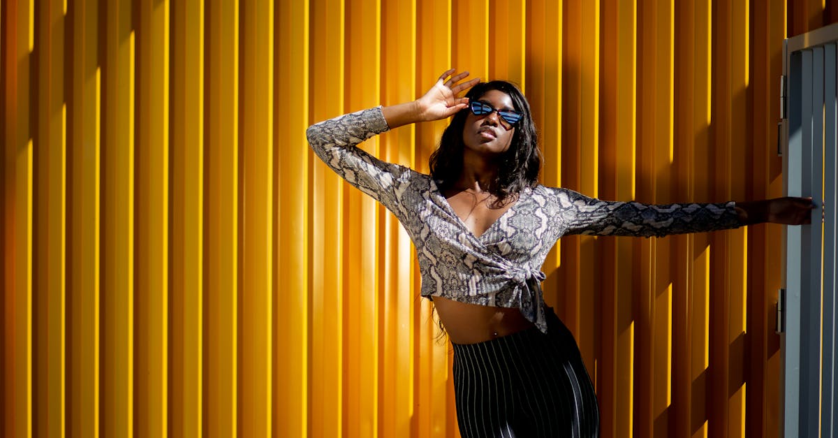 Stylish black woman in crop top and sunglasses posing outdoors against a yellow wall.