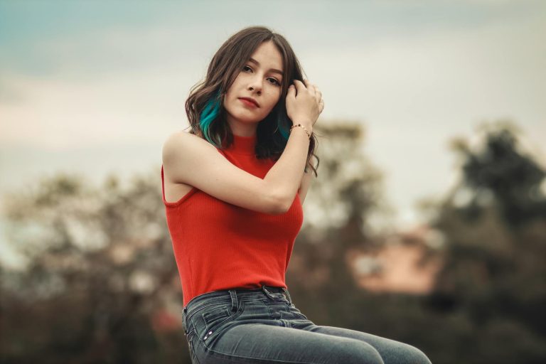 A fashionable young woman poses outdoors with a scenic background.