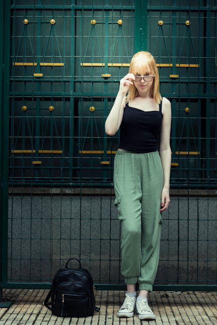 Trendy young woman with eyeglasses posing by a metal gate in São Paulo, Brazil.